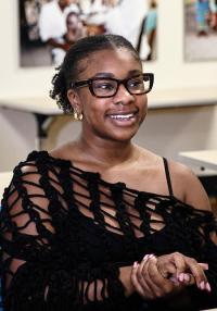 A seated young woman wearing glasses smiles